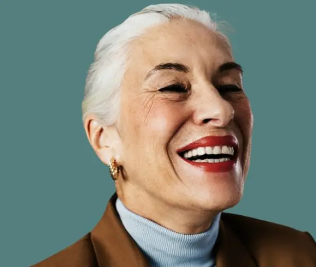 A woman in a blue sweater and white hair, Smiling to showcase the impact of mental health treatment.
